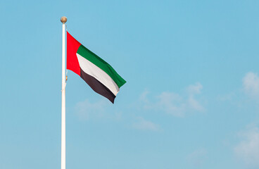 Waving national flag of United Arab Emirates on flagpole, set against a vibrant blue sky, symbolizes pride and identity of the nation