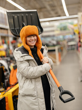 Beautiful smiling woman in winter clothes chose a Large snow shovel in the store. Winter shopping.