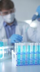 Test tubes with a blue liquid, close-up view. Scientist holding pipette conducting experiments in...