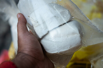A hand holding a plastic-wrapped package of fresh raw tofu, highlighting its smooth texture, white...