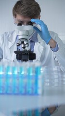 Male scientist researcher wearing lab coat, blue protective gloves, medical mask and glasses, is...