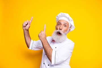 Expressive senior chef gesturing and posing in uniform against yellow backdrop showcasing culinary joy
