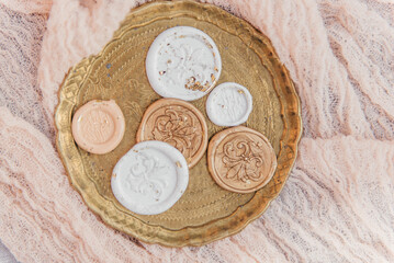 Aesthetic flat lay composition featuring a vintage golden tray with intricate engravings, holding elegant wax seals in white and peach tones with delicate floral designs. 
