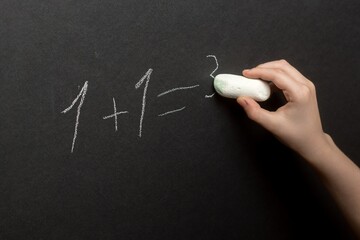 Hand writing '1+1=3' on blackboard with chalk, educational concept, close-up.