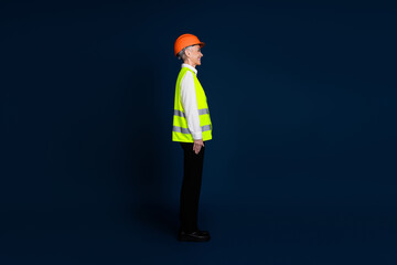 A mature female professional wearing a reflective vest and orange hardhat stands against a dark blue background