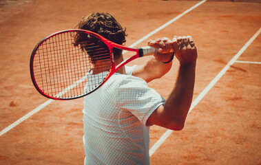 A person holding a tennis racket, preparing to hit a ball on a clay court. The image is taken from...