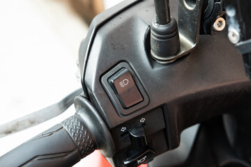 A close-up of a high-beam and low-beam headlight switch on a black scooter or motorcycle, highlighting its textured button and placement on the handlebar