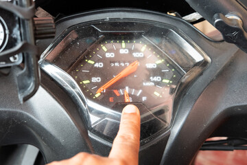A close-up of a scooter or motorcycle speedometer with an index finger pointing at the dial, highlighting the dashboard details and instrumentation