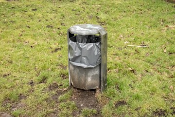 Metal trash can standing on grass in public park