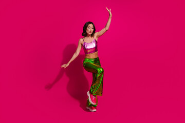 Stylish young woman in glossy outfit posing with vibrant magenta background, showcasing trendy...