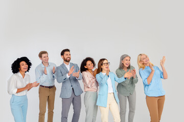 Diverse group of professionals in a friendly atmosphere, smiling and clapping together on a grey...