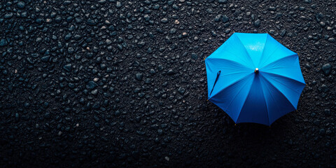 This image showcases a vibrant blue umbrella resting on a dark, textured surface, creating a striking contrast that captures attention and evokes a sense of solitude.