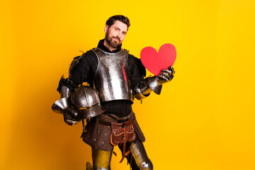Fototapeta premium Medieval knight in shiny armor holds a heartshaped symbol against yellow background