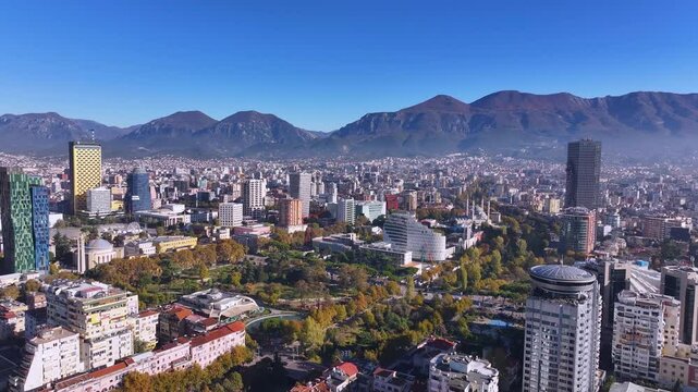 An aerial view of Tirana showcases the city's vibrant landscape, with Mount Dajt towering on the horizon. The mix of modern architecture, green spaces, and bustling streets creates a dynamic urban.