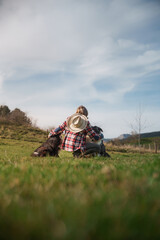 Female farmer kneeling in grassland embracing two border collies. Senior woman farmer petting her two border collies in a green meadow on a sunny day, enjoying the peaceful countryside