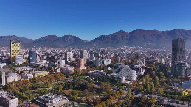 An aerial view of Tirana showcases the city's vibrant landscape, with Mount Dajt towering on the horizon. The mix of modern architecture, green spaces, and bustling streets creates a dynamic urban.
