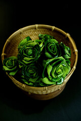 Pandan leaf folded into the flower shape placed on woven basket with black background. Close-up Thai pandan leaves with warm light. Pandan plants, tropic, flavoring, and Asian culture in dark theme.