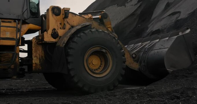 Wheel loader loads coal into wagons. Heavy machinery is working on coal loading at sorting site. Tractor shovels coal with bucket. Sorting and loading of Anthracite. Slow motion shipment coal