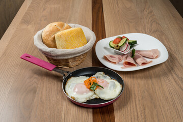 Fried eggs in a skillet bread rolls ham slices and a fresh salad make a perfect breakfast setup