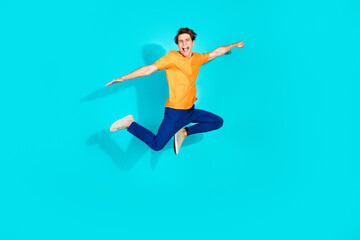 Fototapeta premium Happy young man in vibrant outfit jumping in front of a teal background, expressing positivity and energy