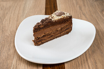 Delicious chocolate cake slice with rich layers and toppings on a clean white plate on a wooden table