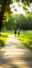 Obraz premium Two children run joyfully along a sunlit wooden path surrounded by vibrant green grass and trees, enjoying a beautiful day in the park