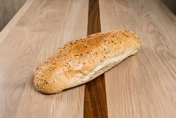 Artisan bread loaf golden brown and coated with seeds displayed on a modern wooden table top
