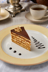 Sumptuous Esterhazy Cake Slice with Rich Chocolate Glaze and Walnut on Elegant Plate Setting