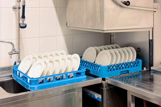 A close-up view of clean white plates stacked in an automatic professional dishwasher machine in the restaurant kitchen.