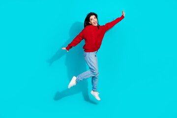 Energetic young woman in stylish casual outfit jumping joyfully against a vibrant turquoise background, expressing excitement