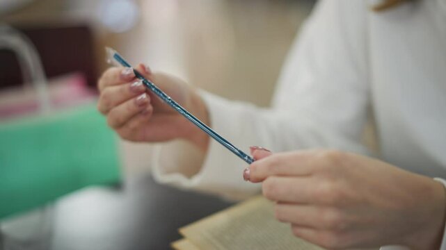 Close-up of hands holding a blue straw while observing it carefully, background features a blurred shopping scene with mint and green shopping bags