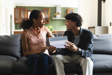 Celebrating success, teen showing acceptance letter to woman on living room couch, at home