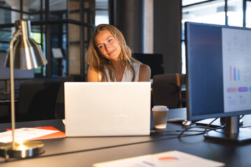 Businesswoman smiling while video conferencing on laptop in modern office at night
