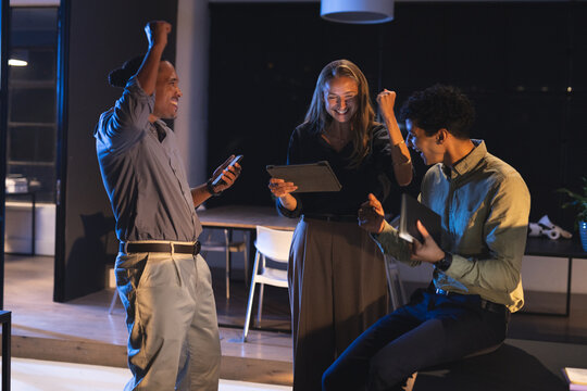 Celebrating success, diverse team using tablets and smartphone in modern office