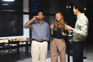 Diverse colleagues enjoying drinks and laughing together during office celebration at night