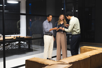 Diverse colleagues toasting with drinks in modern office during late-night meeting
