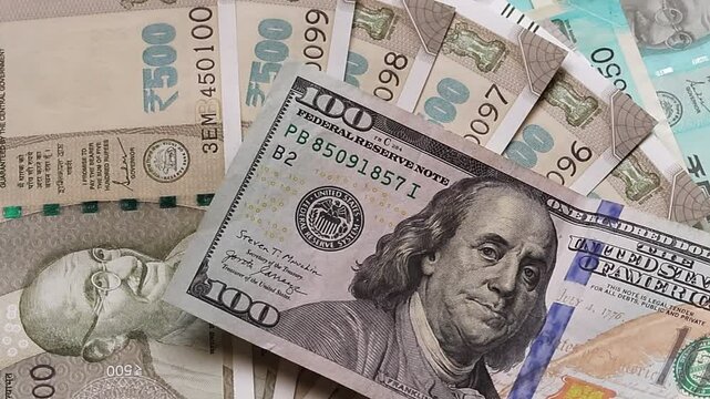 A person places one hundred American dollar banknotes on a table surface with Indian rupee notes of different denomination. Slow motion footage