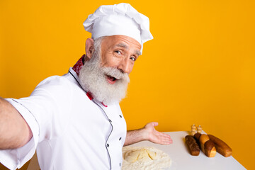 Cheerful senior chef presenting dough and baked goods in a vibrant kitchen setting