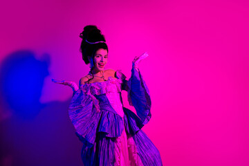 Elegant woman in violet historical dress posing under bright neon lights with pink and purple background