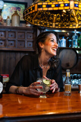 Bartender smiling and holding gin and tonic at wooden bar counter