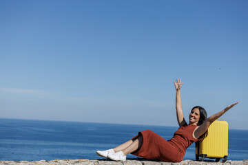Young woman celebrating the beginning of her vacation with her yellow suitcase, recently arrived at the place of her trip, days of fun, happiness, heat, beach, tourism await her...
