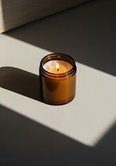 High-Angle View of Lit Dark Amber Glass Jar Candle on Beige Surface with Strong Diagonal Shadow and Dark Brown Background – Minimalist Composition