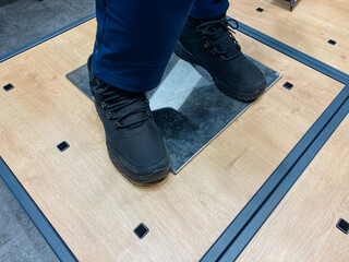 A person wearing black shoes is standing firmly on a polished wooden floor, showcasing the contrast...