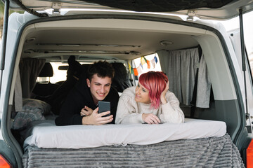 Young couple relaxing in camper van, enjoying mobile lifestyle and using smartphone