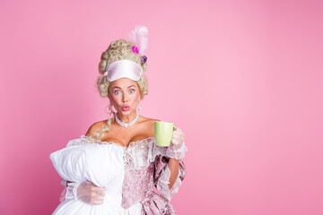 Elegant woman dressed in historical costume holding pillow and mug on vibrant pink background