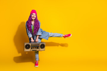 Obraz premium Young playful woman holding a boombox against a vivid yellow background showing style, energy, and vibrant colors
