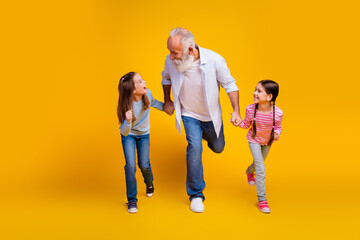 Fototapeta premium Grandfather joyfully playing with two grandchildren on vibrant yellow background, expressing love, fun, and family connection through bonding in casual wear