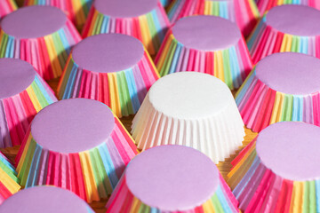 Single white muffin cup among many rainbow cups. Difference concept