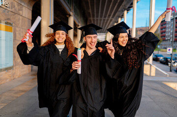 Group of cheerful multi ethnic graduates wearing gowns and holding diplomas, celebrating their...