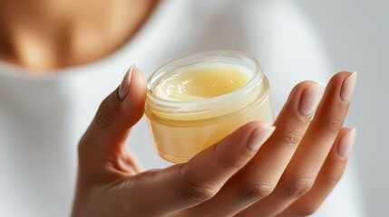 Closeup of woman applying light yellow skincare jelly from jar in clean studio setting